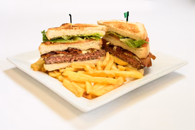 Cheeseburger Club cut in half: toasted bread, burger, bacon, cheese, lettuce and tomato, with fries
